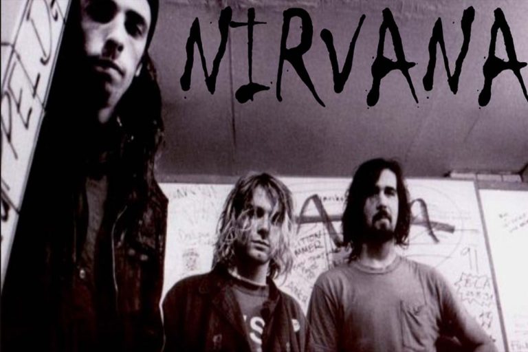 Foto em preto e branco dos integrantes do Nirvana — Kurt Cobain, Dave Grohl e Krist Novoselic — em frente a uma parede pichada, representando a estética sombria e autêntica do movimento grunge.