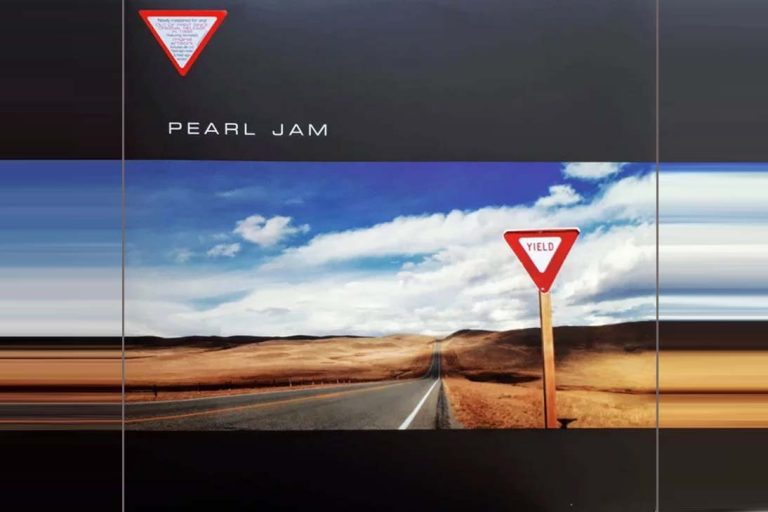 Capa do álbum Yield do Pearl Jam, com uma placa de "dê a preferência" numa estrada deserta.
