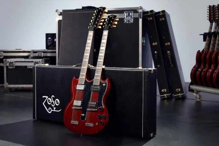 Guitarra Gibson EDS-1275 de dois braços, modelo Jimmy Page, encostada em um case com o símbolo "Zoso", em estúdio cercado por estojos e guitarras.
