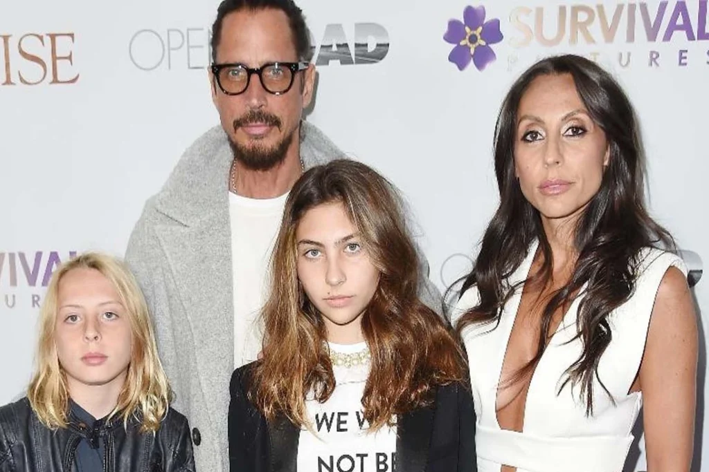 Chris Cornell ao lado de sua esposa e filhos em um evento público, posando para fotos em um fundo promocional.