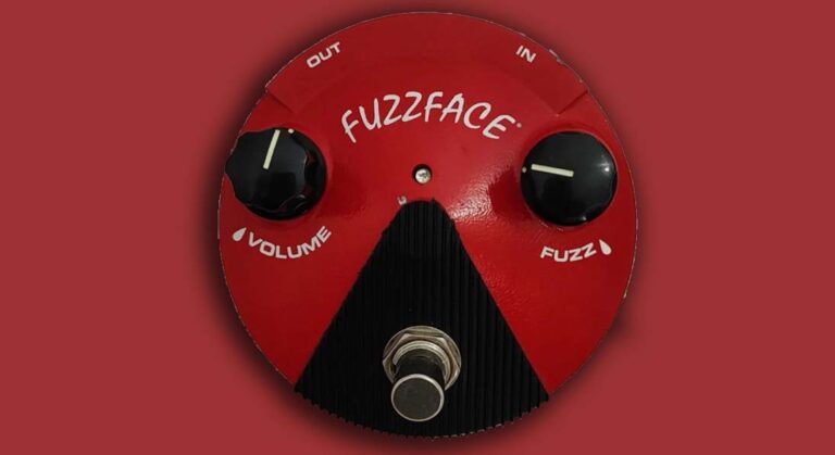 Pedal fuzz face vintage sobre fundo escuro com guitarra elétrica ao fundo mostrando conexões e controles.