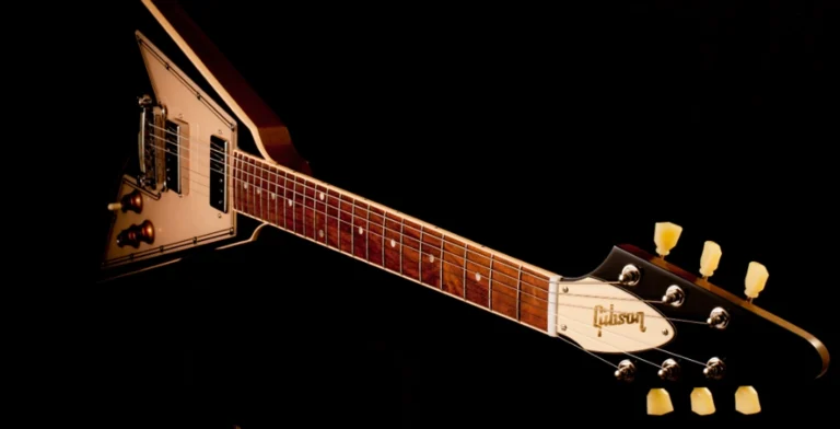 Guitarra Gibson Flying V com corpo em formato de V e acabamento clássico, fotografada em fundo petro.