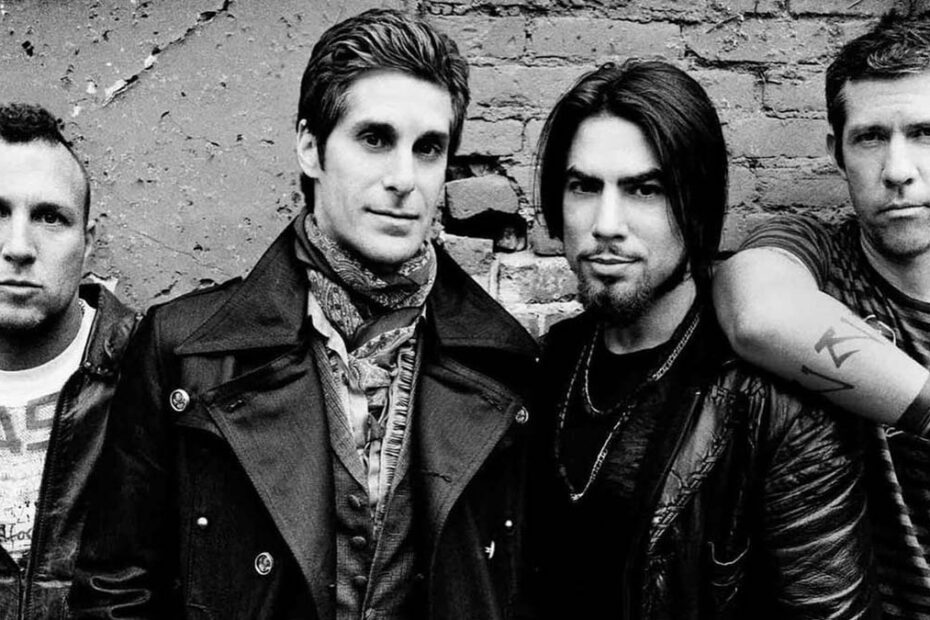 Foto em preto e branco dos integrantes da banda Jane's Addiction posando em frente a uma parede de tijolos.