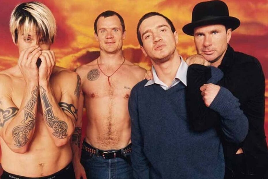 Integrantes da banda Red Hot Chili Peppers posando juntos em frente a um fundo colorido.