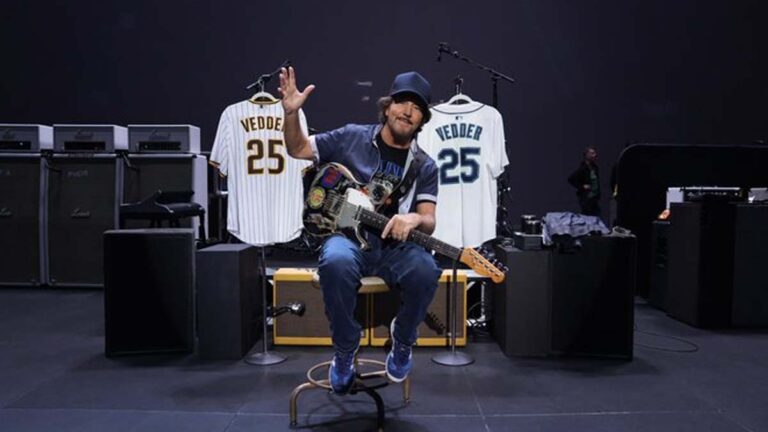 Eddie Vedder sentado com guitarra entre camisas dos Mariners e Padres no Vedder Cup.