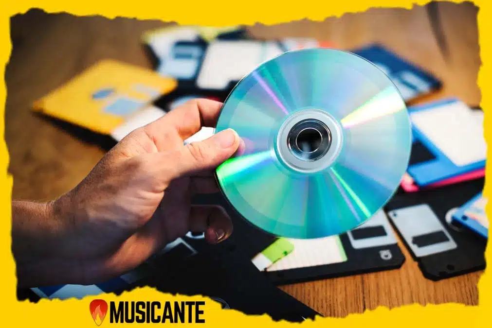 Mão segurando CD compact disc com disquetes e capas de álbuns musicais ao fundo representando evolução da música.